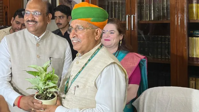 Shri Arjun Ram Meghwal holding a sapling with others at a public function.